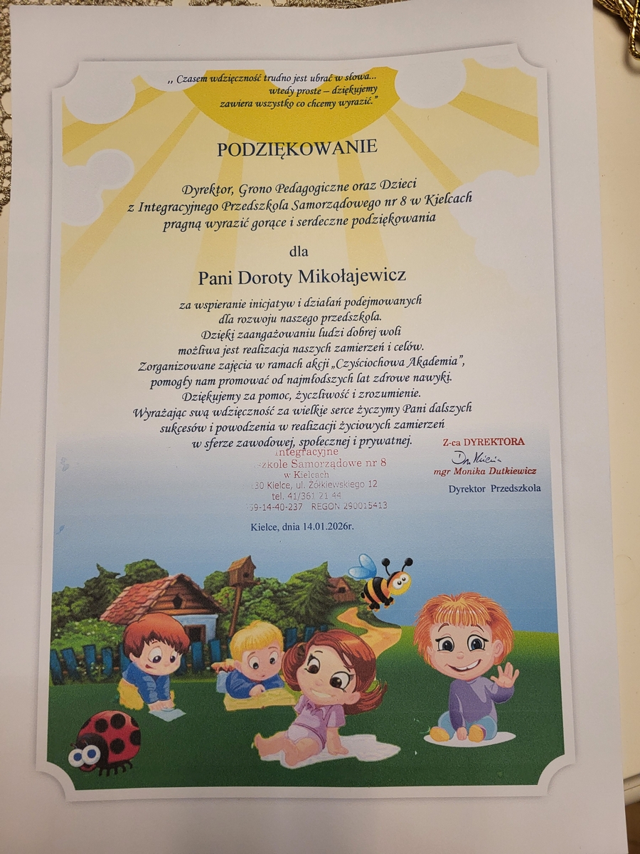 Na obrazie znajduje się dyplom z kolorowymi ilustracjami. W górnej części widoczny jest polski tekst na dekoracyjnym żółto-białym tle z motywem promieni. Całość otacza jasnoszara, ozdobna ramka. Tekst zapisano formalną czcionką. Poniżej przedstawiono ilustrację dzieci siedzących na trawie, obok owadów. W tle widać domy, drzewa oraz niebo.