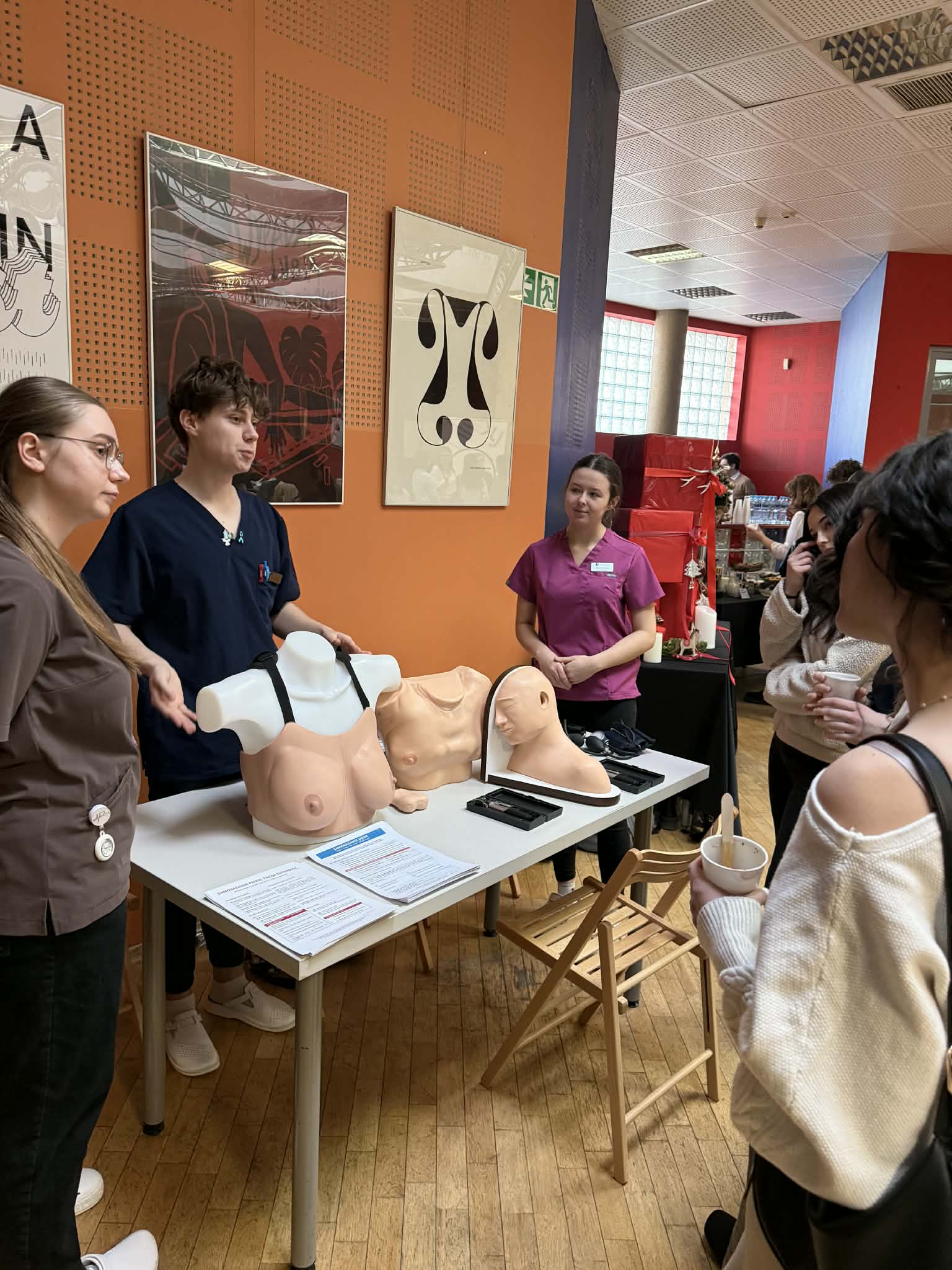 3 osoby stoją obok stołu ma którym są modele sztuczne ludzkie