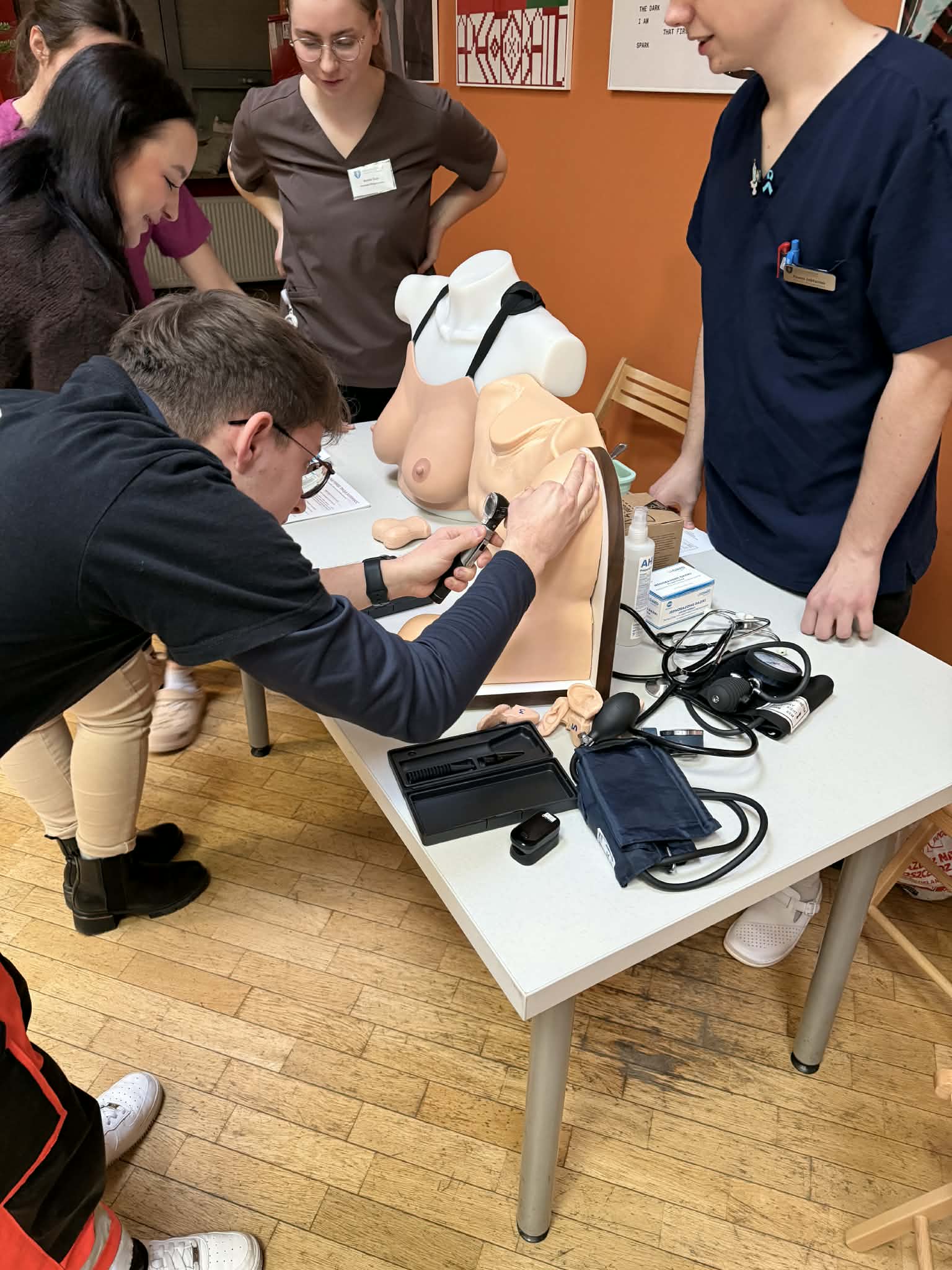 4 osoby obok stołu wykonują badania na modelu człowieka. Na stole sprzęt medyczny