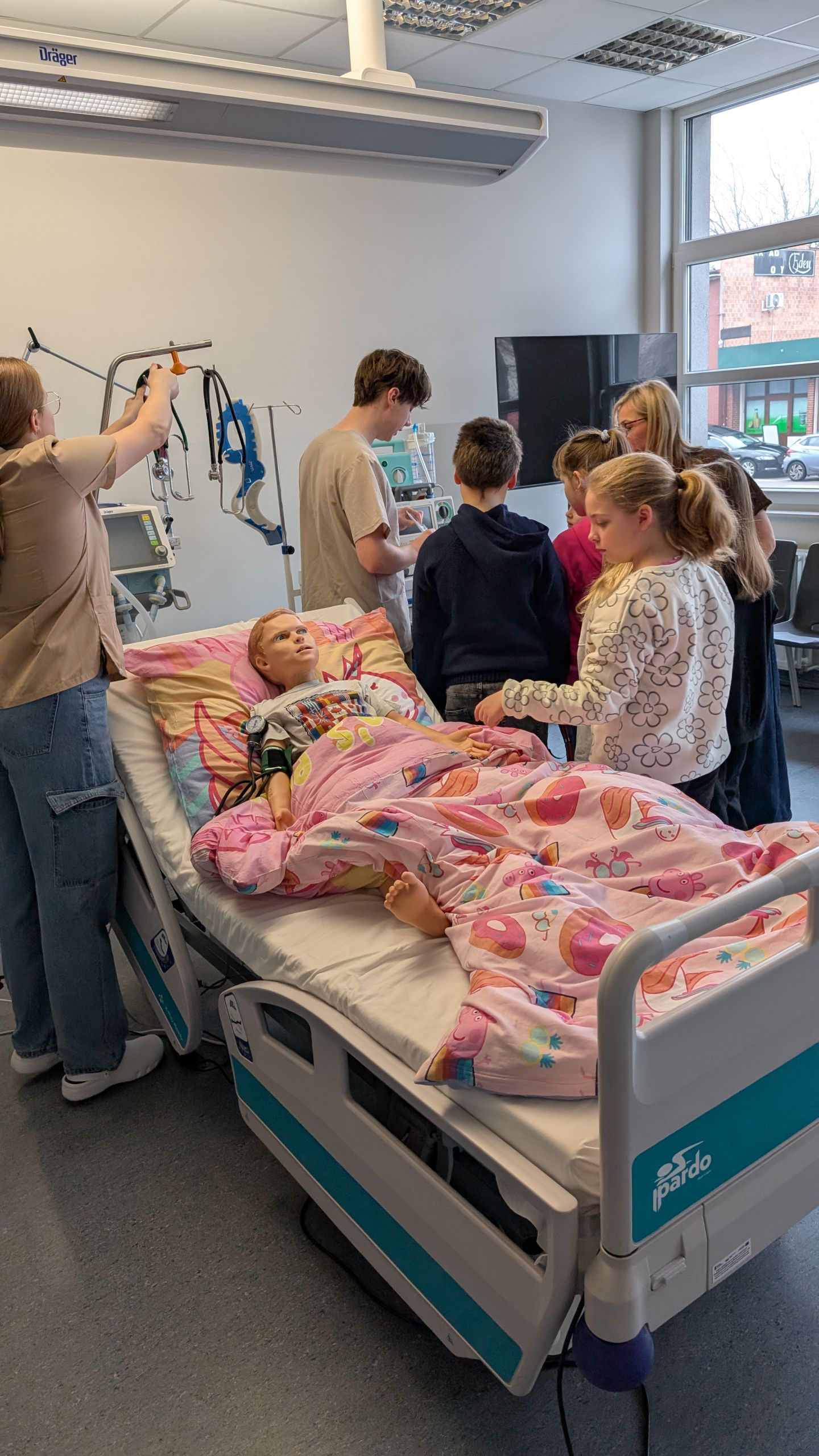 grupa dzieci w sali CSM, lóżko z manekinem