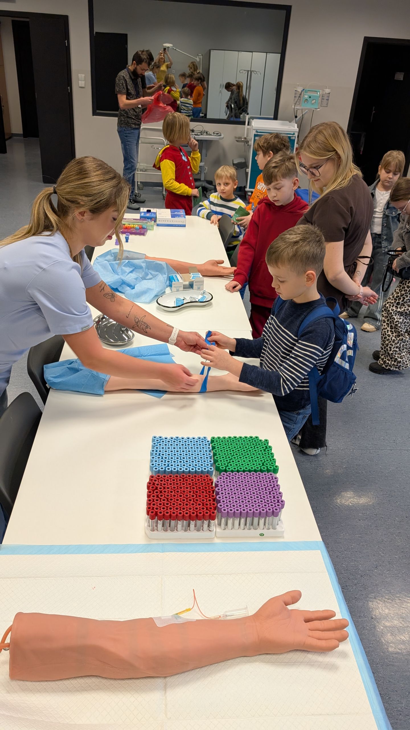 grupa dzieci w sali CSM. Na stole modele rąk i probówki