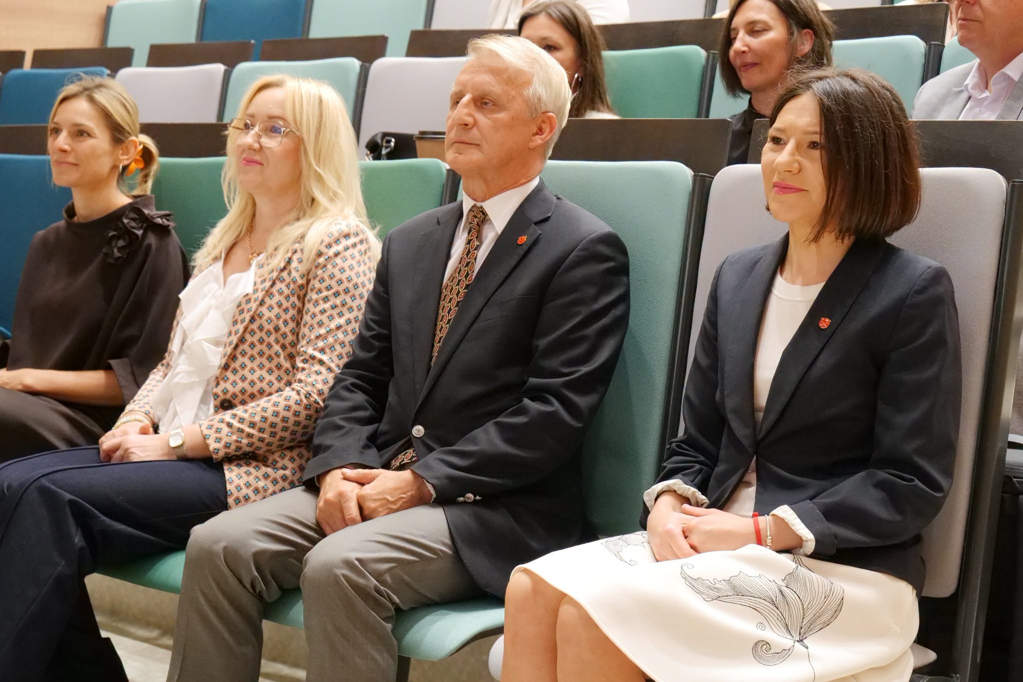 Uczestnicy wydarzenia siedzą na widowni sali audytoryjnej podczas wykładu lub prezentacji. W pierwszym rzędzie widoczne są osoby biorące udział w spotkaniu, a w tle pozostali uczestnicy wydarzenia. Zdjęcie przedstawia moment trwania konferencji, szkolenia lub spotkania edukacyjnego.