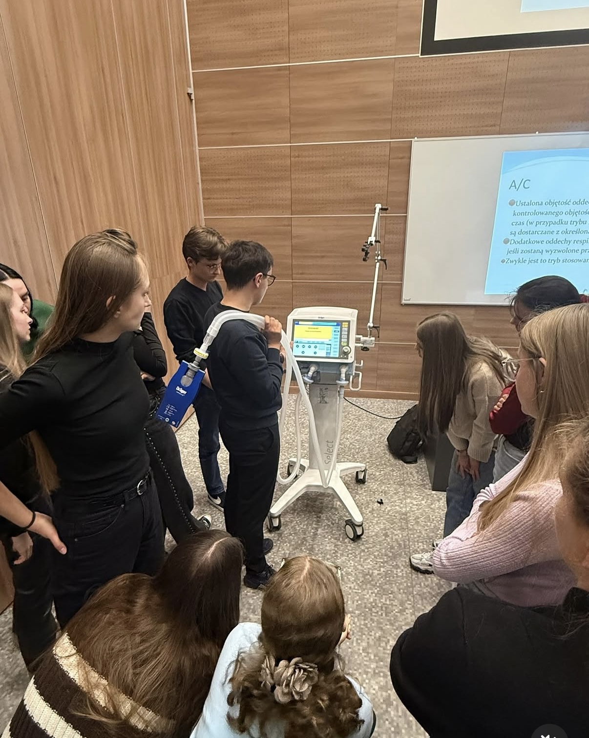 Zdjęcie przedstawia uczestnik&oacute;w zajęć zapoznających się z obsługą respiratora podczas szkolenia. Ćwiczenia prowadzone są z wykorzystaniem specjalistycznej aparatury medycznej wykorzystywanej w ratownictwie i intensywnej terapii. Fotografia ukazuje praktyczną naukę obsługi nowoczesnego sprzętu medycznego.