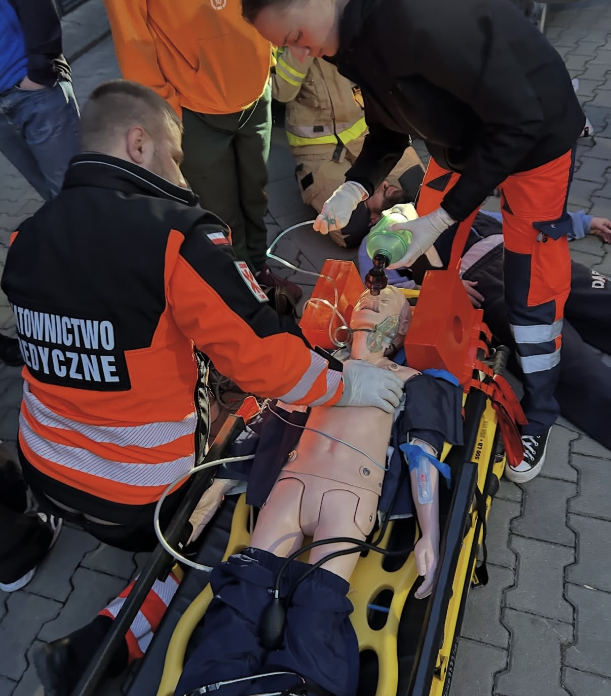 Zdjęcie przedstawia ćwiczenia z zakresu ratownictwa medycznego z wykorzystaniem fantomu szkoleniowego. Uczestnicy doskonalą procedury udzielania pomocy oraz prowadzenia działań ratunkowych przy użyciu specjalistycznego sprzętu. Fotografia ukazuje praktyczną naukę postępowania w sytuacjach zagrożenia życia.