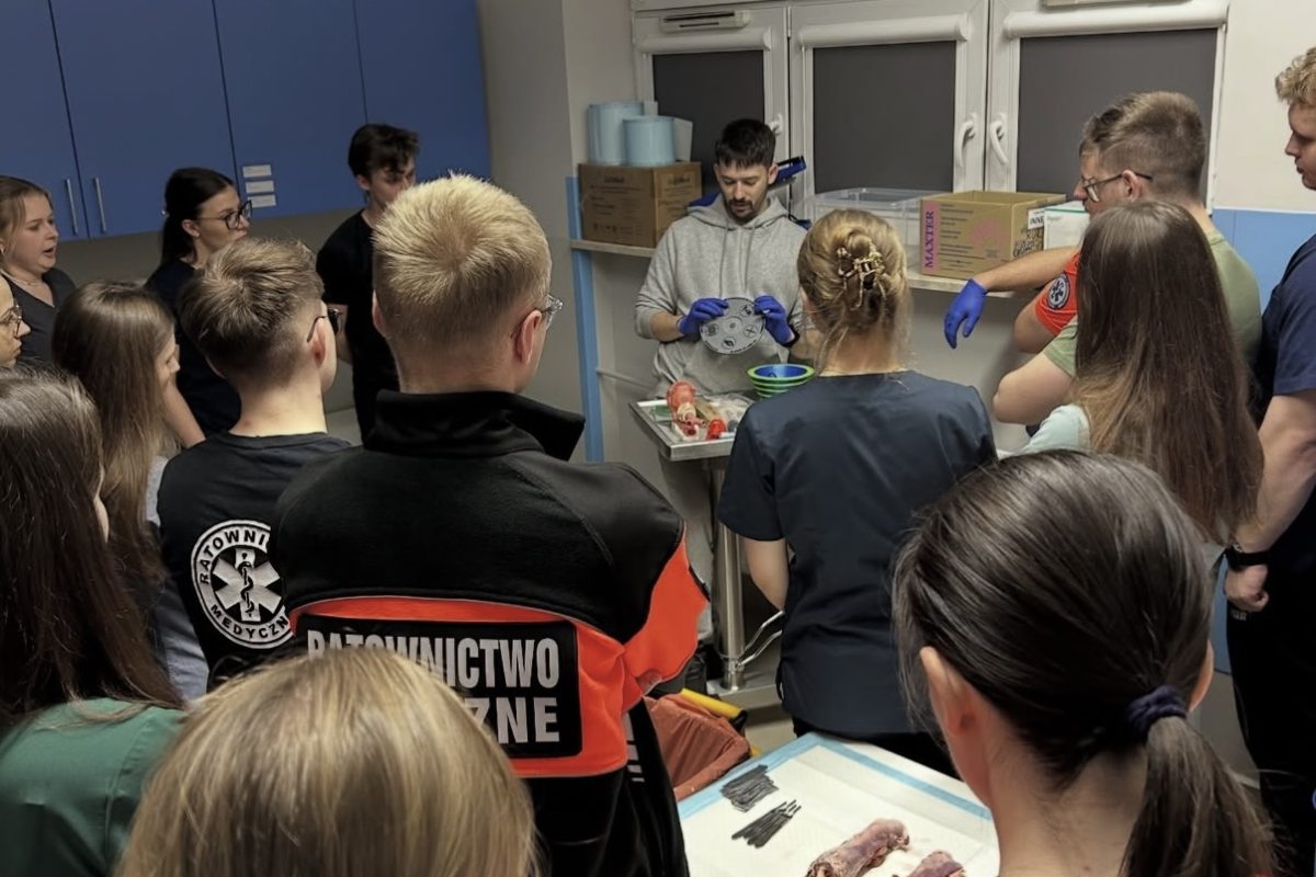 Zdjęcie przedstawia prowadzącego prezentującego procedurę podczas zajęć laboratoryjnych. Uczestnicy obserwują pokaz z wykorzystaniem materiału biologicznego, specjalistycznych narzędzi oraz wyposażenia dydaktycznego. Fotografia ukazuje praktyczną naukę anatomii i procedur medycznych w warunkach laboratoryjnych.