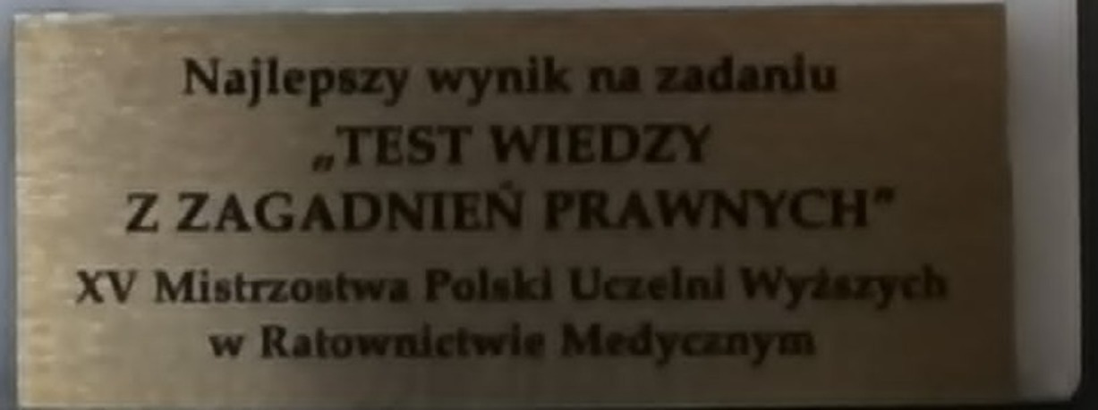 Zdjęcie przedstawia pamiątkową tabliczkę wykonaną z metalu o szczotkowanym wykończeniu. Na jej powierzchni umieszczono grawerowany tekst o charakterze okolicznościowym. Tabliczka stanowi element upamiętniający lub wyróżniający ważne wydarzenie bądź osiągnięcie.