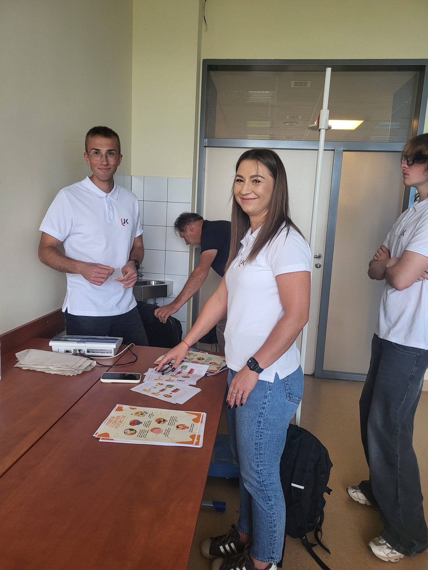 Zdjęcie przedstawia uczestników podczas zajęć lub spotkania w sali dydaktycznej. Na stole znajdują się materiały edukacyjne, sprzęt pomiarowy oraz inne wyposażenie wykorzystywane podczas zajęć. Fotografia ukazuje pracę uczestników z materiałami i specjalistycznym sprzętem.
